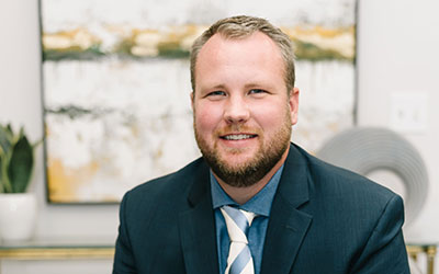 Professional headshot of Drew Parkinson, smiling in a dark suit and striped tie, in an office setting.